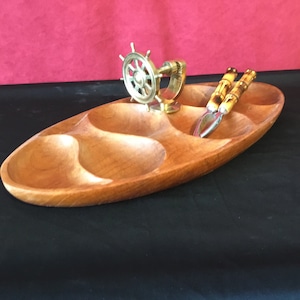 May include: Wooden serving tray with three compartments, featuring a brass ship's wheel and nutcrackers with bamboo-style handles. The tray is light brown and has an oval shape.