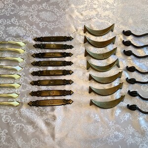 Peut inclure: Assortiment de quincaillerie d'armoire vintage, comprenant 8 poignées de tiroir dorées, 6 poignées de tiroir en laiton et 6 poignées de tiroir noires avec des accents en forme de feuille.