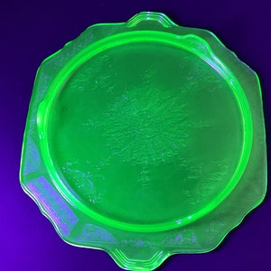 May include: A green glass plate with a scalloped edge and a floral design. The plate is made of uranium glass and glows under a black light.