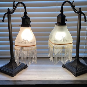 May include: Two black metal table lamps with frosted glass shades and beaded fringe. The shades have a delicate etched design.