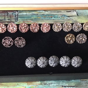 Könnte beinhalten: Sortiment an dekorativen Metall-Schubladengriffen in verschiedenen Ausführungen, darunter Kupfer, Bronze und Silber. Die Griffe haben verzierte Designs mit floralen Motiven.