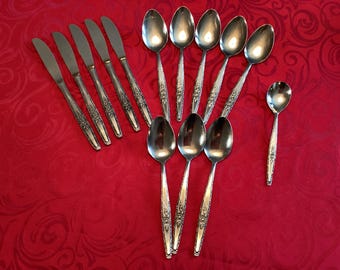 Puede incluir: Una colección de cubiertos de acero inoxidable, que incluye cucharas y cuchillos, dispuestos sobre un mantel rojo estampado. Los cubiertos tienen mangos decorativos. La imagen muestra un juego de utensilios de comedor.