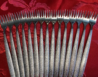 May include: A set of 18 silver-toned forks with textured handles. The forks are arranged in a fan shape on a red background.