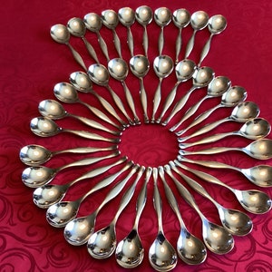 May include: A collection of shiny, silver spoons arranged in a circular pattern on a red tablecloth. The spoons have a classic design with rounded bowls and slender handles. The arrangement creates a visually appealing display.