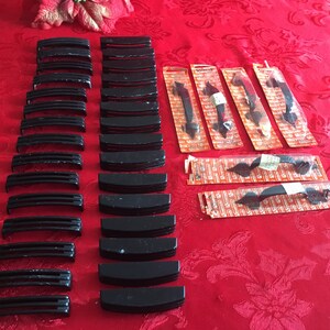 Puede incluir: Una colección de herrajes de gabinete negros, que incluyen tiradores de cajones y pomos de puerta, dispuestos sobre un mantel rojo. El herraje está empaquetado en bolsas de plástico transparentes con etiquetas naranja y blancas.