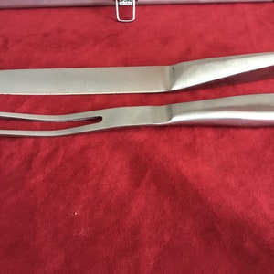 Puede incluir: Un juego de trinchar plateado con un cuchillo y un tenedor. El juego está sobre una superficie roja.
