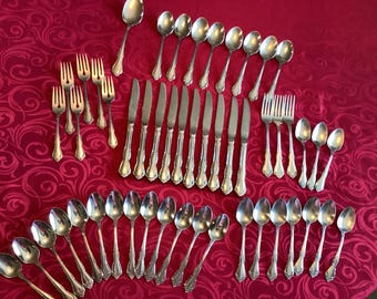 May include: A collection of vintage silverware, including forks, knives, and spoons, arranged on a red patterned tablecloth. The silverware has ornate handles and a shiny, reflective surface, suggesting a formal dining setting.