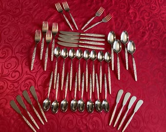 May include: A complete set of vintage silverware, including forks, knives, spoons, and butter knives, arranged on a red tablecloth. The silverware has a textured handle design. The set includes serving spoons and butter knives.