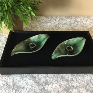 Puede incluir: Dos candelabros de cerámica en forma de hoja, de color verde y marrón, en una caja forrada de terciopelo negro.