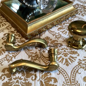 May include: Two polished brass door levers with curved handles and a single matching round brass door knob. The hardware features a smooth, reflective metallic finish and circular mounting plates with visible screw holes for installation.