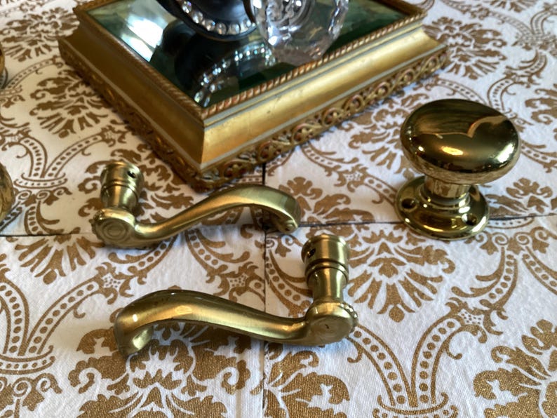 May include: Two polished brass door levers with curved handles and a single matching round brass door knob. The hardware features a smooth, reflective metallic finish and circular mounting plates with visible screw holes for installation.