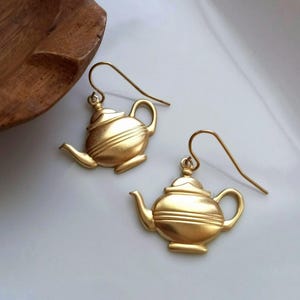 May include: A pair of gold-tone teapot dangle earrings. The earrings are made of metal and have a detailed teapot design.