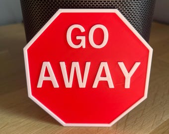 Puede incluir: Un objeto rojo y blanco con forma de señal de stop con las palabras "GO AWAY" en letras blancas. El letrero tiene un borde blanco y está sobre un fondo borroso.