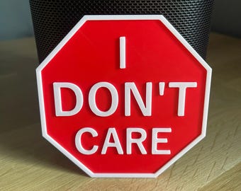May include: A red, octagonal sign with white text that reads "I DON'T CARE." The sign has a white border and is reminiscent of a stop sign. The sign is a novelty item.