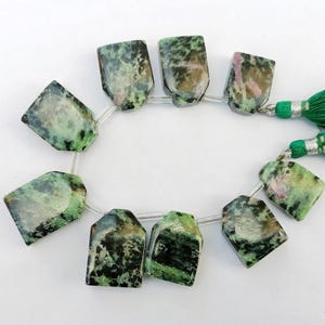 Puede incluir: Hilo de cuentas rectangulares con una mezcla de tonos verdes, negros y rosas. Las cuentas están ensartadas en un cordón transparente y conectadas a una borla verde. Las cuentas miden aproximadamente 3,2 cm de largo.