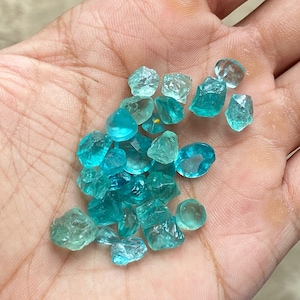 May include: A collection of teal and blue gemstone chips in various sizes and shapes. The chips are loose and scattered on a hand.