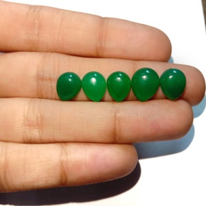 May include: Five green oval-shaped gemstones, likely cabochons, are arranged in a row on a finger.