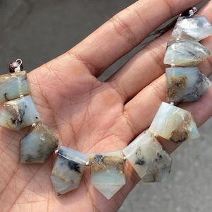 May include: A strand of faceted, irregular, semi-translucent stones in shades of pale blue, white, and gray, featuring dark brown and black dendritic inclusions. Each stone is shaped into a geometric point and strung together with silver accents.