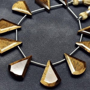 Könnte beinhalten: Eine Kette aus Edelsteinperlen in Tropfenform mit flacher Oberseite und weißem Akzent. Die Perlen sind in Braun- und Beigetönen gehalten und auf einem silbernen Draht aufgefädelt. Geeignet für die Schmuckherstellung.