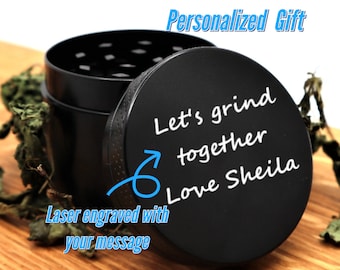 Może przedstawiać: Czarny metalowy młynek z pokrywką, na której wygrawerowano tekst "Let's grind together Love Sheila". Młynek znajduje się na drewnianej powierzchni.
