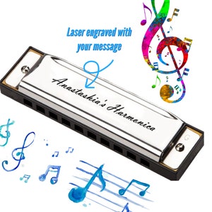 Pode incluir: Uma gaita de boca prateada com uma caixa preta. A gaita de boca é gravada com o texto "Anastasia's Harmonica". A imagem também inclui uma clave de sol colorida e notas musicais.