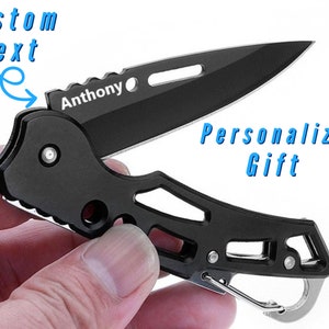 Könnte beinhalten: Schwarzes Taschenmesser mit Karabinerhaken. Das Messer hat eine personalisierte Gravur mit dem Text "Anthony".