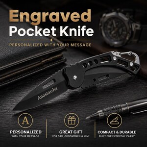 May include: A black folding pocket knife with a skeletonised handle and a carabiner clip. The blade is engraved with the name Anastaisha. The knife features a pointed tip, a sharp edge, and a metallic pivot screw, presented in a sleek design.