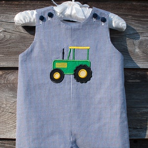 Puede incluir: Un pelele de pana azul y blanco con un diseño de tractor bordado en verde y amarillo.