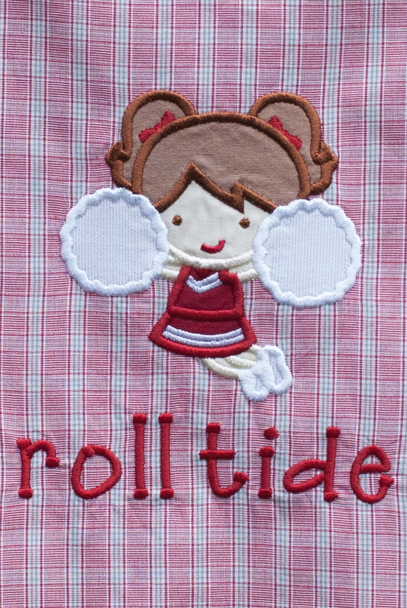 May include: Embroidered design of a cheerleader with brown hair, a red and white uniform, and white pom-poms. The text "roll tide" is embroidered in red on a red and white plaid background.