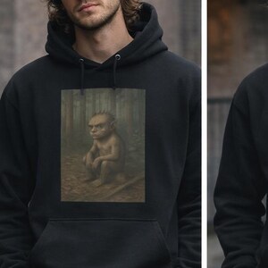 May include: Black hooded sweatshirts with different fantasy art prints. One features a forest creature, another a person watching a UFO, and the third a creature with glowing red eyes. The sweatshirts are worn by a person wearing a black cap and khaki pants.