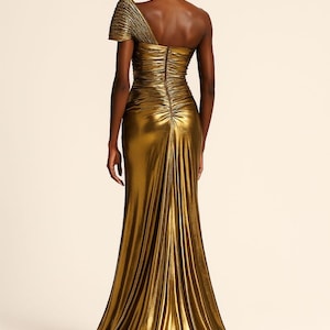 Pu&ograve; includere: Un abito da sera dorato monospalla con gonna lunga fino al pavimento. L'abito presenta un corpetto arricciato e un design drappeggiato e fluido. Il tessuto ha una lucentezza metallica, creando un look glamour. L'abito &egrave; adatto per eventi formali.