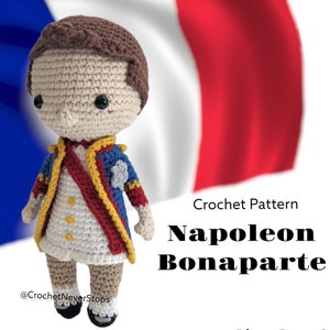 K&ouml;nnte beinhalten: H&auml;kelanleitung f&uuml;r eine Napoleon Bonaparte Amigurumi-Puppe. Die Puppe tr&auml;gt eine blaue, rote und goldene Uniform mit einem wei&szlig;en Hemd. Die Puppe steht vor einer franz&ouml;sischen Flagge.