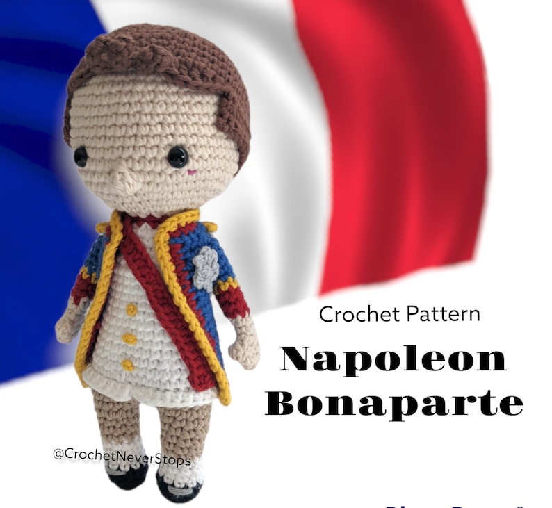 K&ouml;nnte beinhalten: H&auml;kelanleitung f&uuml;r eine Napoleon Bonaparte Amigurumi-Puppe. Die Puppe tr&auml;gt eine blaue, rote und goldene Uniform mit einem wei&szlig;en Hemd. Die Puppe steht vor einer franz&ouml;sischen Flagge.