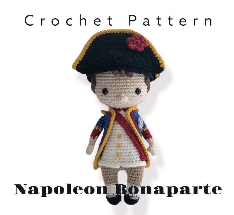 K&ouml;nnte beinhalten: H&auml;kelanleitung f&uuml;r eine Napoleon Bonaparte Amigurumi-Puppe. Die Puppe tr&auml;gt eine blaue und goldene Uniform mit einer roten Sch&auml;rpe und einen schwarzen Hut mit einer roten Blume.