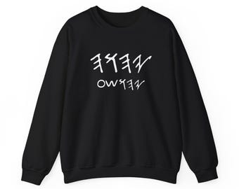 May include: Black crew neck sweatshirt with white Hebrew script. The sweatshirt features two lines of stylized Hebrew letters. The garment is a solid black color, with long sleeves and a classic, casual design.