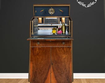 May include: A vintage wooden bar cabinet with a brass base and two doors. The cabinet has a lift-up top with a mirrored interior and a built-in liquor rack. The cabinet is closed and the top is open, revealing the interior.