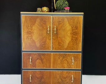 May include: A vintage wooden cabinet with gold accents and black trim. The cabinet has two doors with gold handles and two drawers with gold pulls. The cabinet is sitting on four gold legs.