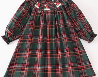 Könnte beinhalten: Ein langärmeliges Kleid mit einem dunkelgrünen, roten und weißen Karomuster. Das Kleidungsstück hat einen gesmokten Ausschnitt, der mit kleinen gestickten roten Weihnachtsmannmützen mit weißem Rand und grünen Stechpalmenblättern verziert ist.
