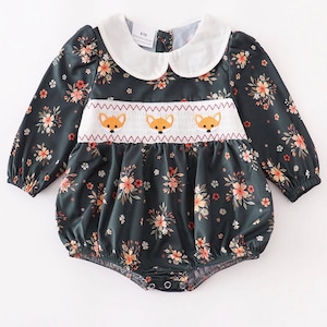May include: A dark green long-sleeve romper featuring a white Peter Pan collar and a smocked chest panel with three embroidered orange fox faces. The fabric has a floral print with orange and white flowers. A tag inside reads 6M.