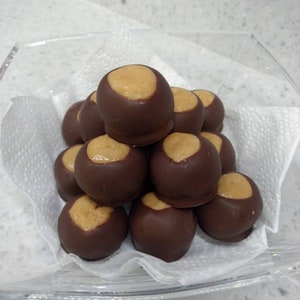 May include: A close-up of a pile of chocolate peanut butter candies in a clear glass bowl. The candies are arranged in a pyramid shape, with the top candy being a peanut butter cup. The candies are all covered in dark chocolate and have a peanut butter filling.