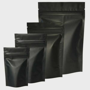 May include: Four black stand-up pouch bags of different sizes are displayed. Each bag has a matte finish and a zip-top closure. The bags are empty and appear to be made of a durable, opaque material. The background is a plain, light grey.