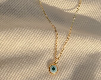 Puede incluir: Un collar de cadena dorada con un pequeño colgante azul de ojo turco.