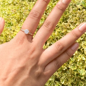 May include: A gold ring with a large, clear, round gemstone surrounded by smaller gemstones. The ring is on a finger.
