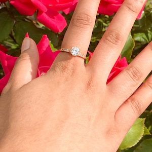 May include: A gold ring with a large, clear, round gemstone surrounded by smaller gemstones. The ring is on a person's finger.