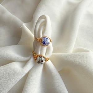 May include: Two gold rings with white ceramic beads. The beads are decorated with blue and black floral patterns.