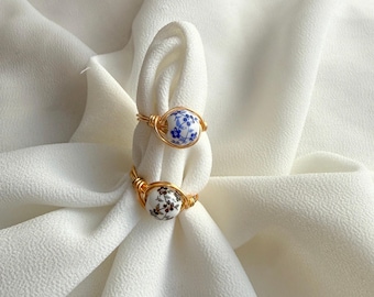 May include: Two gold rings with white ceramic beads. The beads are decorated with blue and black floral patterns.