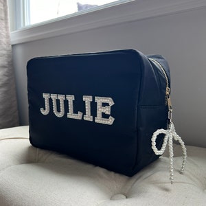 May include: Black zippered wash bag with a pearl-beaded zipper pull. The bag has the name "JULIE" spelled out in white letters with rhinestones.