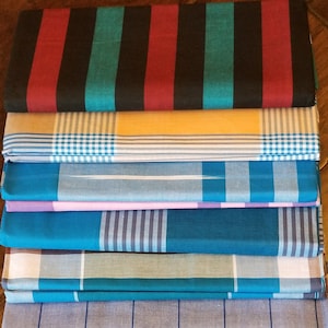 May include: A stack of ten fabric panels with various patterns, including stripes, plaid, and checkered designs. The panels are in shades of blue, red, black, white, and yellow.