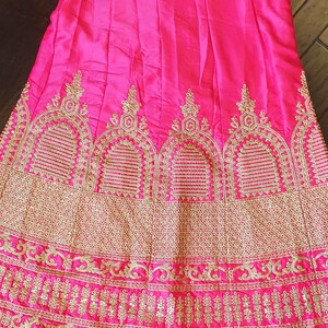 May include: A hot pink skirt with gold embroidery. The skirt has a pleated design and a wide waistband. The embroidery features intricate floral patterns.