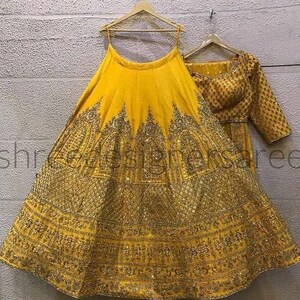 May include: A yellow lehenga with gold embroidery and sequins. The skirt is full and flowing, and the top is a fitted choli with short sleeves.